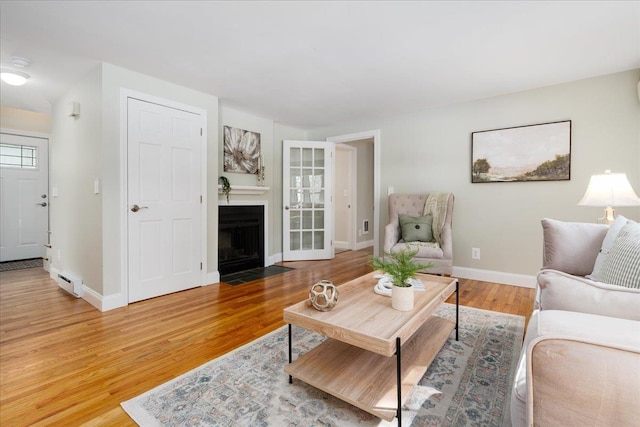 living area featuring a fireplace with flush hearth, baseboards, and wood finished floors