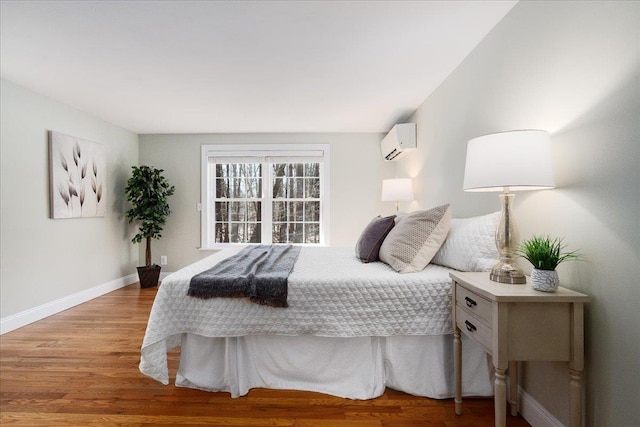 bedroom featuring an AC wall unit, baseboards, and wood finished floors