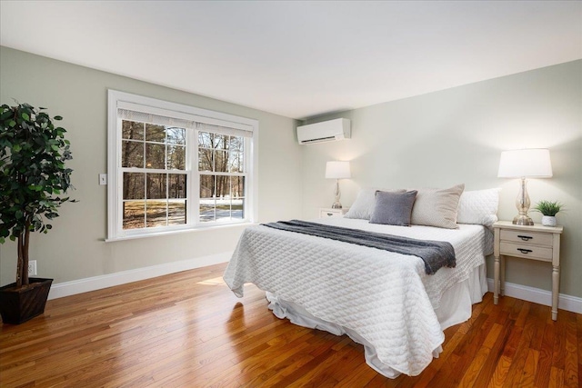 bedroom with baseboards, wood finished floors, and a wall mounted AC