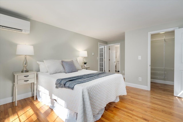 bedroom featuring a walk in closet, an AC wall unit, and light wood finished floors