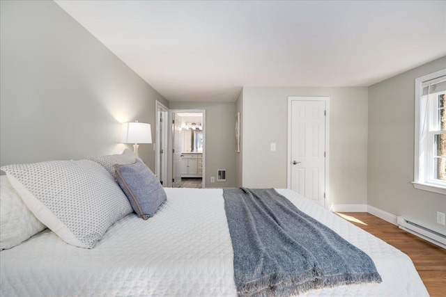 bedroom featuring wood finished floors, visible vents, baseboards, ensuite bathroom, and baseboard heating