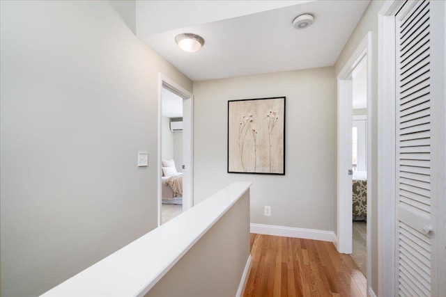 hall featuring an upstairs landing, light wood finished floors, an AC wall unit, and baseboards