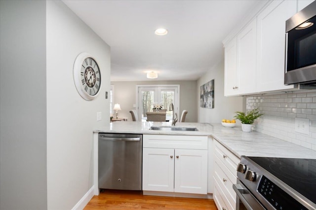 kitchen with light wood finished floors, a sink, stainless steel appliances, white cabinetry, and backsplash