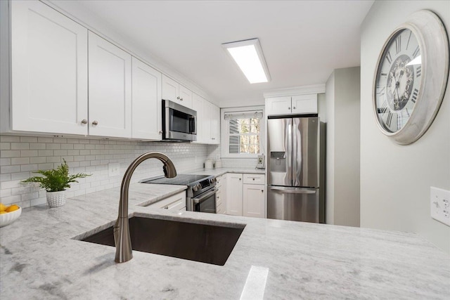 kitchen featuring tasteful backsplash, light stone counters, appliances with stainless steel finishes, white cabinetry, and a sink