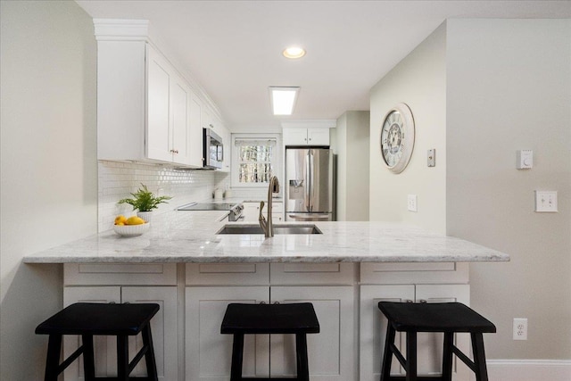 kitchen with backsplash, light stone countertops, a peninsula, stainless steel appliances, and a sink