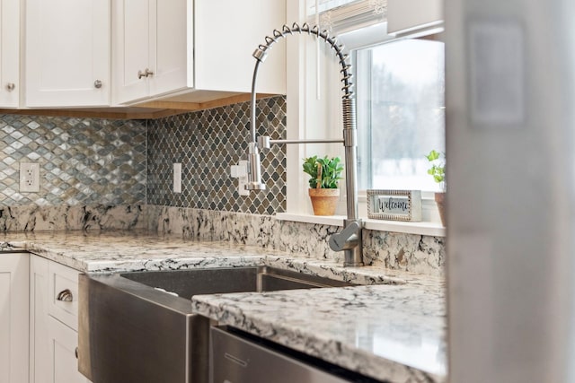 kitchen featuring backsplash, a sink, white cabinets, and light stone countertops