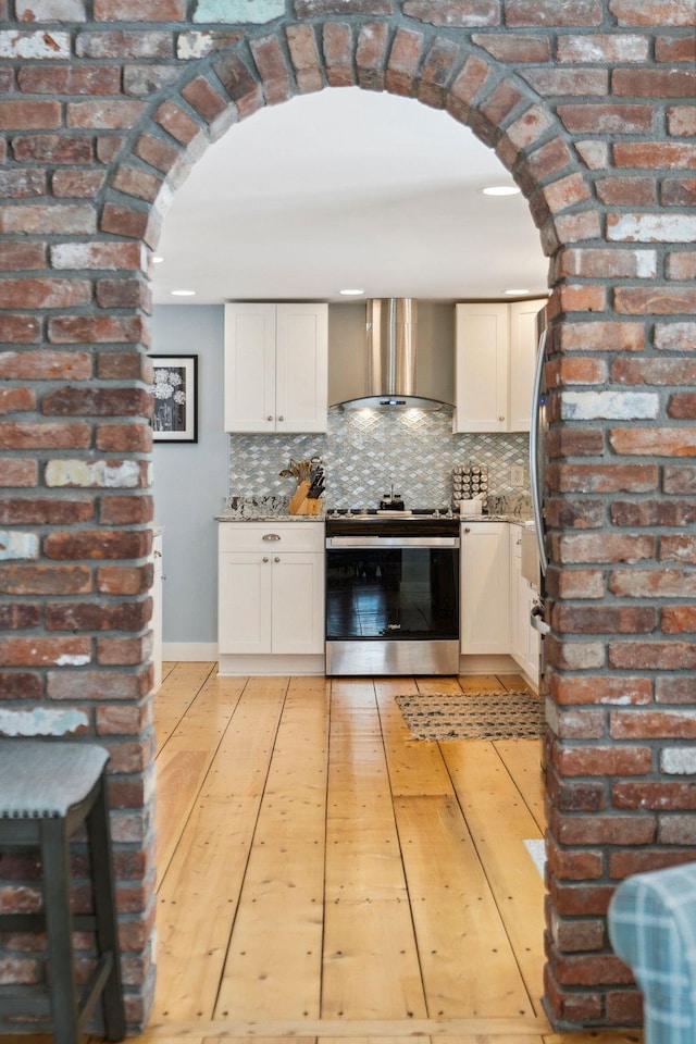 kitchen featuring decorative backsplash, wall chimney exhaust hood, arched walkways, and stainless steel range with electric cooktop