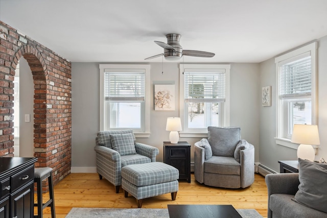 living room featuring a baseboard heating unit, baseboards, a healthy amount of sunlight, and wood finished floors