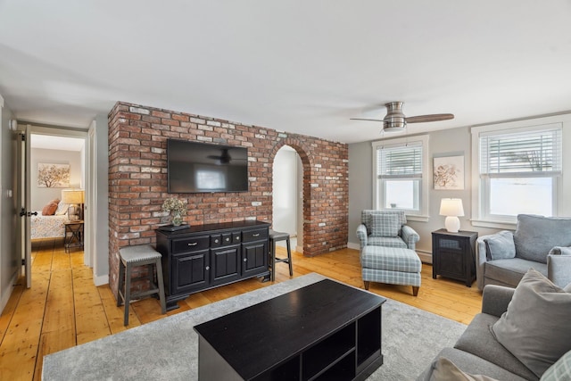 living room with a baseboard heating unit, arched walkways, light wood-style flooring, and a ceiling fan