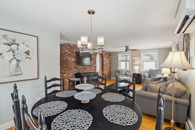 dining area with brick wall, a baseboard heating unit, an AC wall unit, ceiling fan with notable chandelier, and wood finished floors