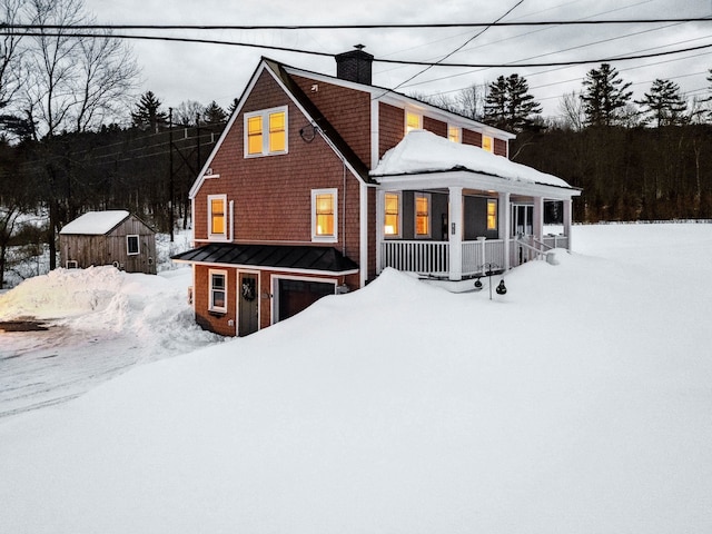 view of front of home with an attached garage, a porch, a chimney, and a standing seam roof