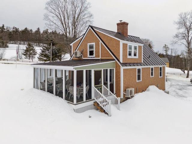 snow covered rear of property with ac unit, a standing seam roof, a sunroom, metal roof, and a chimney