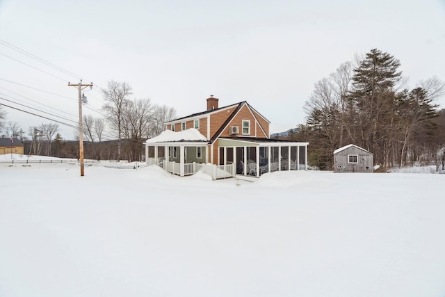 snow covered back of property with a storage shed, an outdoor structure, a chimney, and a sunroom