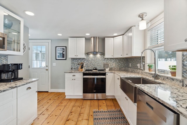 kitchen with white cabinetry, appliances with stainless steel finishes, light wood-style flooring, and wall chimney range hood