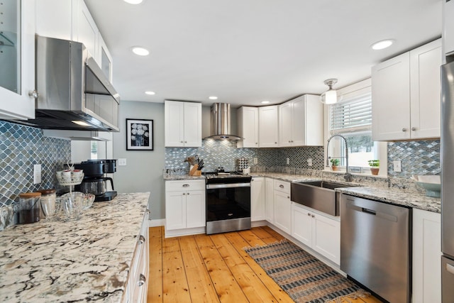 kitchen with light wood-style flooring, a sink, stainless steel appliances, white cabinetry, and wall chimney range hood