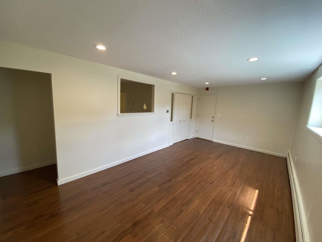 empty room with a baseboard heating unit, baseboards, and dark wood-style floors