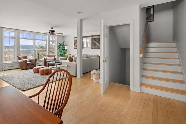 interior space featuring light wood finished floors, stairs, ceiling fan, and a baseboard radiator