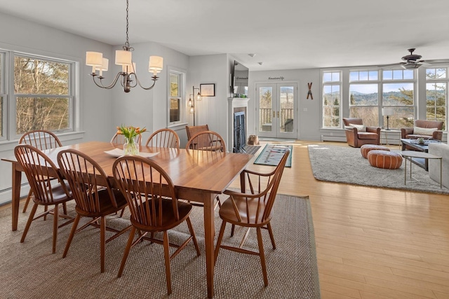 dining space with baseboard heating, ceiling fan with notable chandelier, a fireplace, and wood finished floors