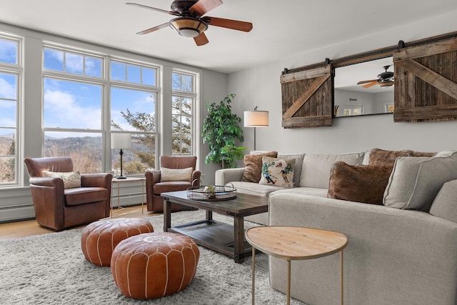 living area featuring ceiling fan, a baseboard heating unit, a barn door, and wood finished floors