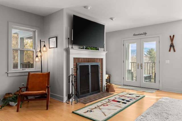 living area featuring a fireplace, wood finished floors, french doors, and baseboards