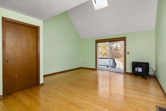 unfurnished living room with light wood finished floors, visible vents, baseboards, lofted ceiling with skylight, and a wood stove