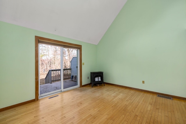 unfurnished room with light wood-type flooring, visible vents, baseboards, and a wood stove