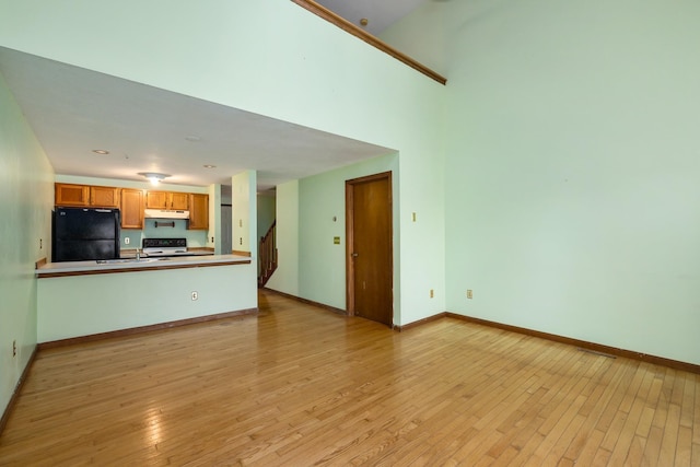 kitchen with baseboards, light wood-style flooring, freestanding refrigerator, range with electric cooktop, and under cabinet range hood