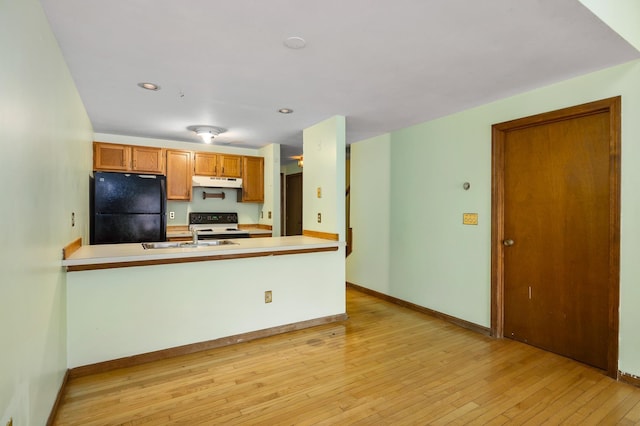 kitchen featuring under cabinet range hood, a peninsula, freestanding refrigerator, light wood-style floors, and a sink