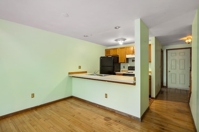 kitchen with light wood-style flooring, freestanding refrigerator, a sink, light countertops, and white range with electric stovetop