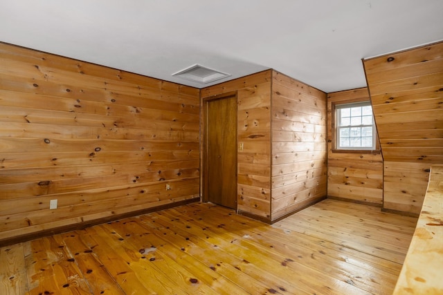 additional living space with light wood-style floors and wood walls