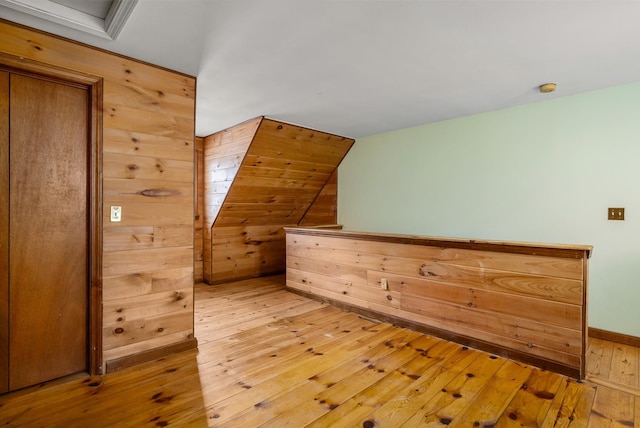 additional living space featuring lofted ceiling, wooden walls, and light wood-style flooring