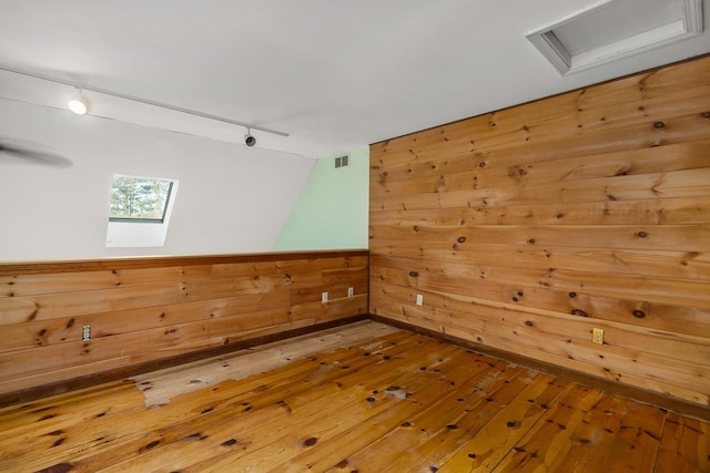 spare room featuring visible vents, attic access, hardwood / wood-style flooring, rail lighting, and wood walls