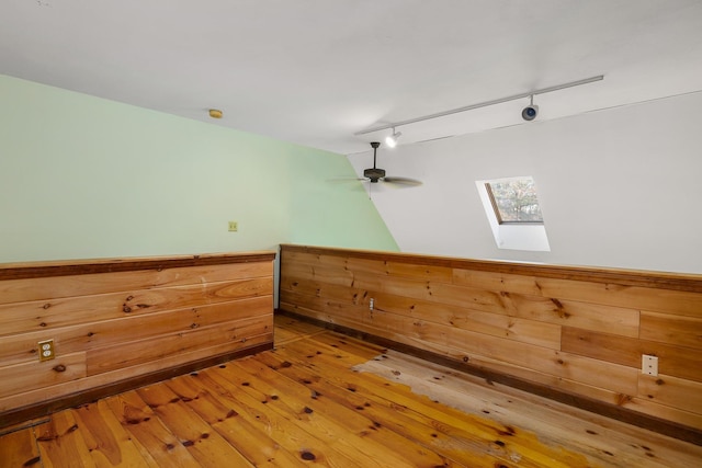 additional living space featuring light wood finished floors, a wainscoted wall, wood walls, and a skylight