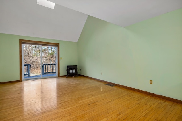 interior space featuring light wood-type flooring, visible vents, a wood stove, and vaulted ceiling