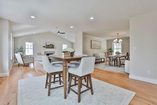 dining area with baseboards, recessed lighting, a fireplace, vaulted ceiling, and light wood-style floors