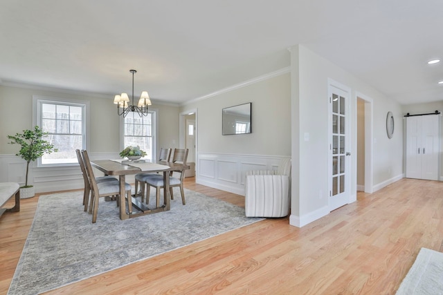 dining space with an inviting chandelier, light wood-type flooring, a barn door, and ornamental molding