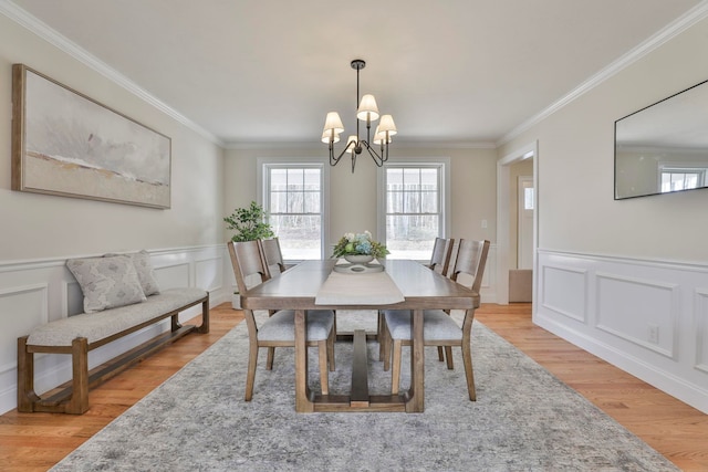 dining space with a wainscoted wall, a notable chandelier, crown molding, and light wood finished floors