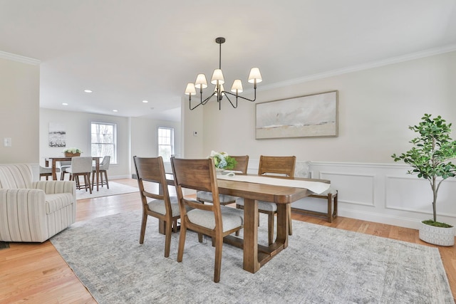 dining room with light wood finished floors, a wainscoted wall, ornamental molding, recessed lighting, and a decorative wall