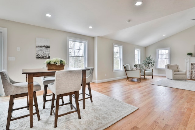 dining area featuring baseboards, lofted ceiling, recessed lighting, a fireplace, and light wood-type flooring