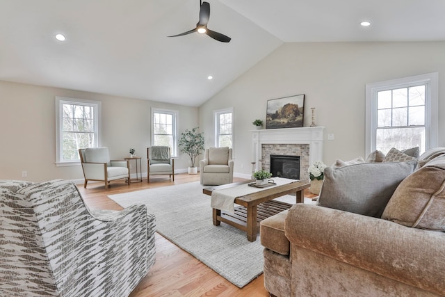 living area featuring lofted ceiling, a fireplace, light wood-type flooring, and ceiling fan