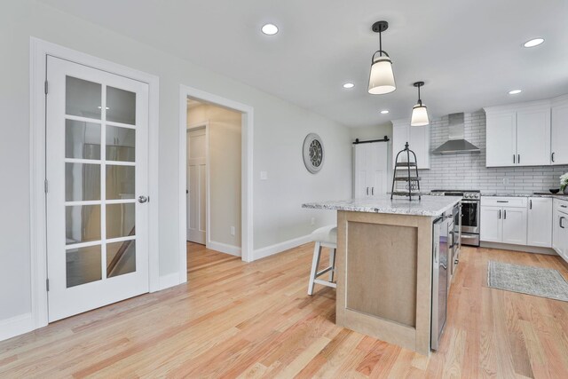 kitchen with light wood-style floors, a barn door, stainless steel range, and wall chimney range hood