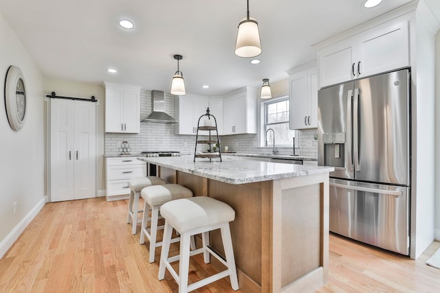 kitchen with a barn door, white cabinets, appliances with stainless steel finishes, and wall chimney range hood