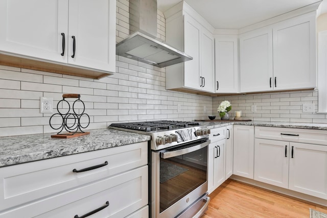 kitchen featuring light wood-style flooring, tasteful backsplash, white cabinetry, wall chimney exhaust hood, and stainless steel range with gas stovetop