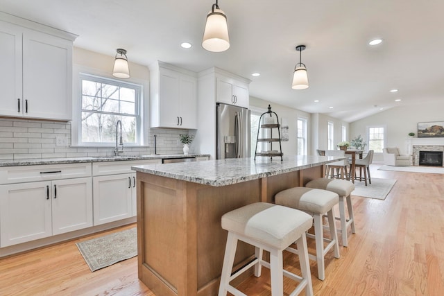 kitchen with a kitchen island, light wood-type flooring, decorative backsplash, stainless steel refrigerator with ice dispenser, and a sink