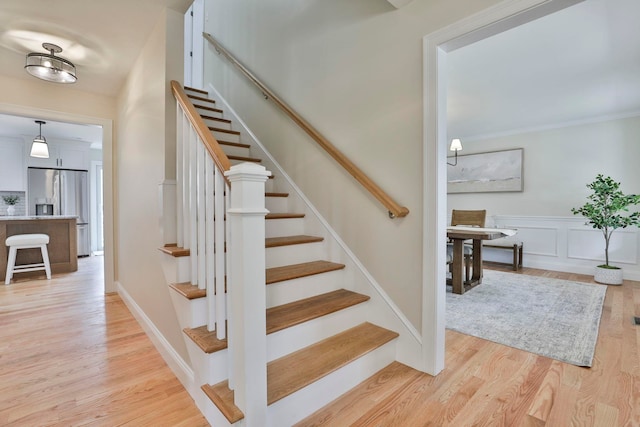 stairway featuring crown molding, a decorative wall, wood finished floors, and wainscoting