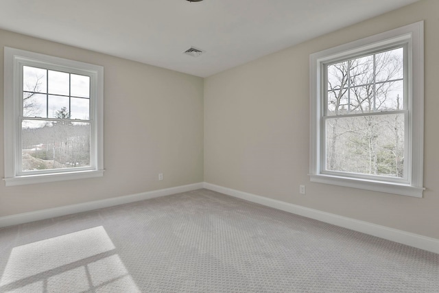 carpeted spare room featuring plenty of natural light, baseboards, and visible vents