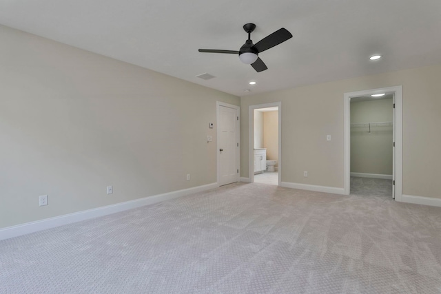 unfurnished bedroom with a walk in closet, light carpet, recessed lighting, connected bathroom, and baseboards