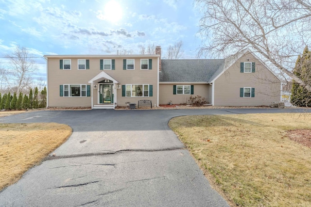 colonial house with aphalt driveway, a chimney, and a front lawn