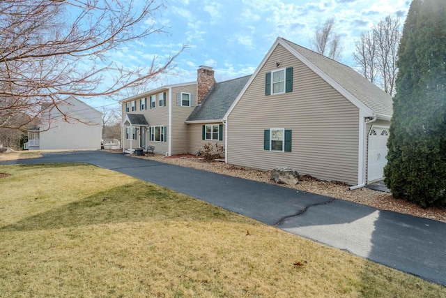 rear view of property with a yard, a garage, roof with shingles, and a chimney