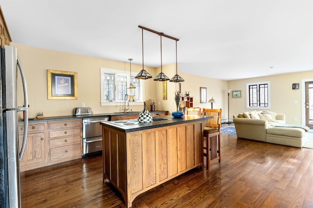 kitchen featuring dark countertops, dark wood-style floors, appliances with stainless steel finishes, and a kitchen bar